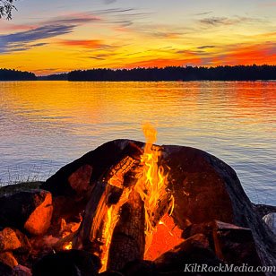 A campfire in the foreground of a setting sun with fantastic colours. This landscape shot was taken as part of the filming of the 'Landscape Theatre - Lakefront' series by KiltRockMedia.com.