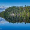 A beautiful calm, blue lake with the island and a fallen birch tree in the foreground. This landscape shot was taken as part of the filming of the 'Landscape Theatre - Lakefront' series by KiltRockMedia.com.
